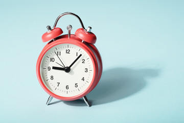 Red alarm clock with shadow on blue background. Seven minutes past nine on the clock