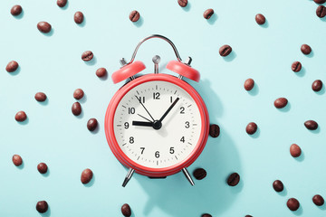 Red alarm clock and roasted coffee beans on blue background with shadow. Concept of morning...