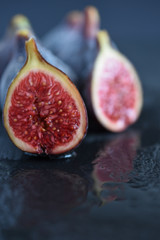 Top view of the red interior of a fig, reflected in water, with more unfocused figs, on black background