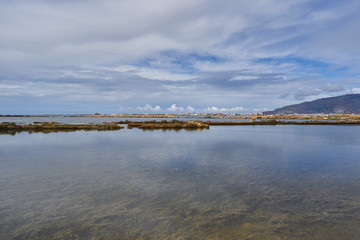 Landscape picture of saltpans in traditional salt production close to sicilian city Trapani in italy with mountain of Erice and Trapani harbour in background. Picture takn in sunny cloudy summer day.