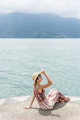 woman with hat sit at a pier