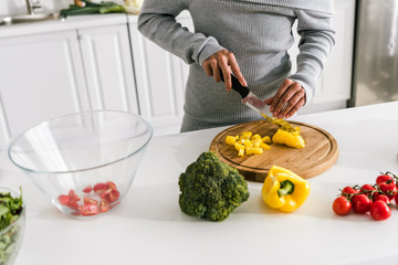 cropped view of woman cutting yellow paprika near cherry tomatoes and broccoli