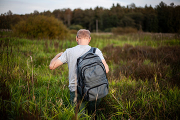 Naklejka na ściany i meble A man walks across the field. Traveler moves on rough terrain. In search of plants. A guy with a backpack walks in nature.