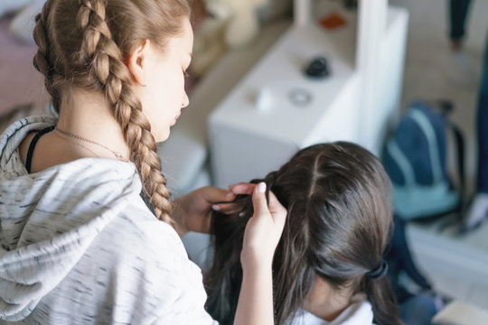 friend making pigtail hair of teen girl in apartment house