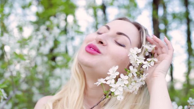Face of a beautiful blonde woman close-up. She strokes a branch with flower buds in the garden.