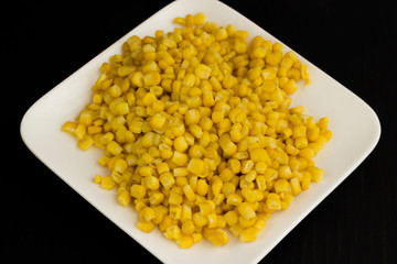 Boiled corn on a white plate. Black background