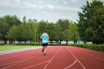 Young, adult alone man running fast on red stadium track. Enjoying sport in summer. Daily active lifestyle. Life motion. Back view.