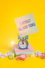 Text sign showing I Attract All Good Things. Business photo showcasing Positive attraction law Motivation Affirmation Alarm clock sticky note paper balls stacked notepads colored background