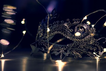 A portrait of a venetian mask in the evening full of mystery on a wooden table surrounded by lights. It is perfect to hide someones identity on a masked ball.