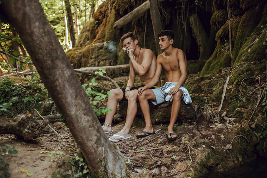 Two bare chested friends smoking a joint of marijuana in nature
