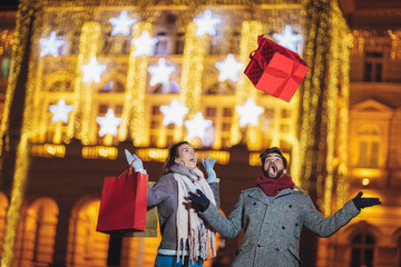 Fototapeta premium Young couple in the city centre with holiday's brights in background. Man presenting gift to woman, having fun.