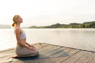 Young woman practicing yoga on a jetty at a lake