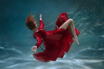 Beautiful slender girl in a long red dress underwater. - obrazy, fototapety, plakaty