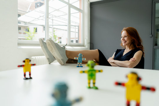 Portrait of redheaded woman in a loft with miniature robots on desk