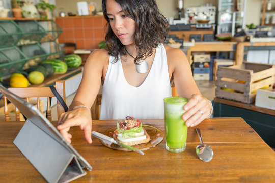 Young woman in organic store, using tablet, eating healthy snack