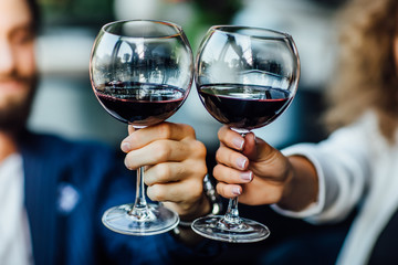 Beautiful young couple with glasses of red wine in luxury restaurant, close up photo.