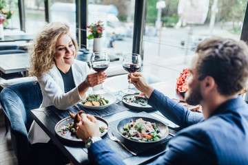 Romantic pretty young couple at restaurant raising a toast. Beautiful couple with glasses of red...