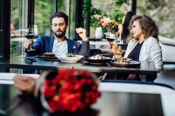 Romantic pretty young couple at restaurant raising a toast. Beautiful couple with glasses of red wine in restaurant. Lifestyle.
