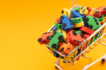 mini toy rubber cars in supermarket trolley on yellow background