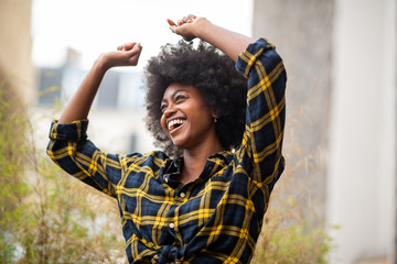 cheerful young carefree afro woman with arms raised and smiling outside - Powered by Adobe