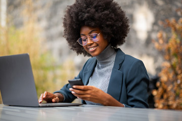 young african american business woman smiling with with laptop and mobile phone - Powered by Adobe