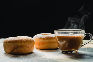 A cup of coffee with smoke smoldering and donuts in the kitchen, Morning Nature light by window on wood table, Black background,  Selective focus, Homemade food and hot beverages are good for health.