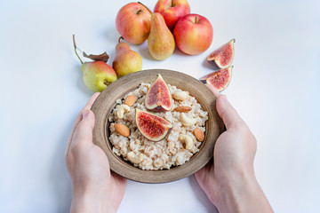 Oatmeal in a bowl with fresh figs, almonds and cashews. Oatmeal with fruits. Men's hands hold a bowl of porridge. White background.