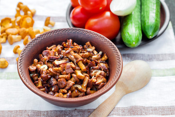 Fried chanterelles with onion in rustic bowl and plate with fresh vegetables for salad on background