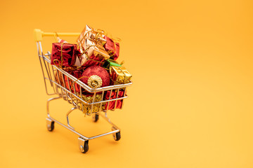 New Year's gifts and toys in supermarket trolley on yellow background. Christmas shopping concept