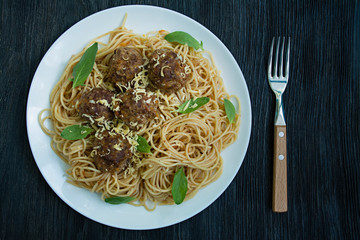 Pasta with meatballs and parsley in tomato sauce. Dark wooden background. View from above.