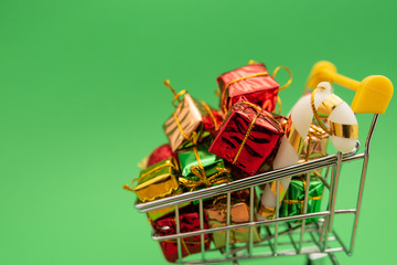 New Year's gifts and toys in supermarket trolley on green background. Christmas shopping concept