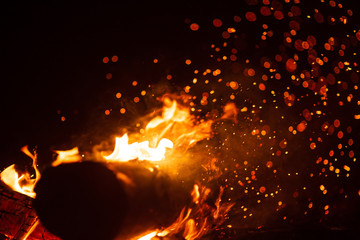 Fototapeta na wymiar Beautiful abstract background on the theme of fire, light and life. Burning red hot sparks fly from large fire in the night sky. Burning embers glowing flying over black background.