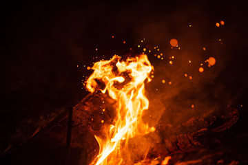 Beautiful abstract background on the theme of fire, light and life. Burning red hot sparks fly from large fire in the night sky. Burning embers glowing flying over black background.