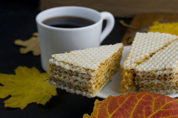  a white plate with triangular slices of waffle cake with a white cup of coffee in defocus and red and yellow leaves scattered on the table