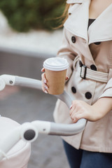 Close up photo, woman holding disposable coffee cup and staying at baby stroller.