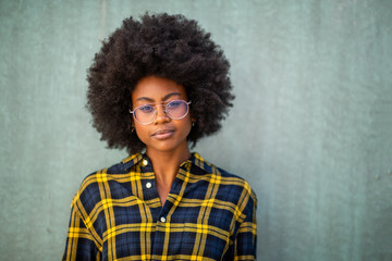 Close up front of beautiful young african american woman with glasses against green wall