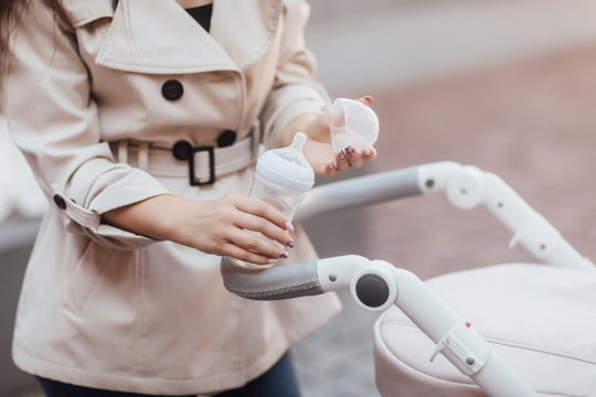 Baby food and water. Young mother is going to feed the baby with a bottle of baby drink. Happy woman walking with a stroller. Close-up young mother, pram, baby food and drink in the bottle.