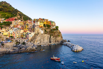 Fototapeta na wymiar Panorama of Manarola in Cinque Terre, La Spezia. Colorful buildings near the ligurian sea. View on boats moored in marina with blue water at sunset.