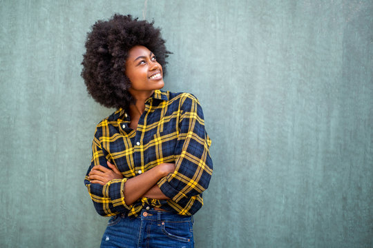 smiling young african american woman with afro hair standing arms crossed and looking up