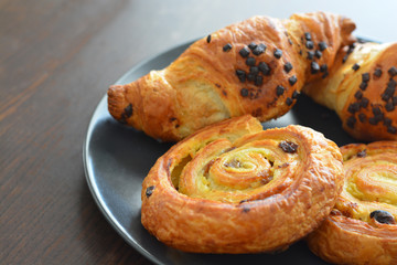 Danish raisin swirls and chocolate hazelnut croissants on a black plate. French pastry.