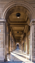 Arcade (arched passageway) in Bologna, Italy, with stone columns casting long shadows on the shiny...