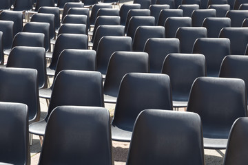 Rows of empty black plastic chairs (seats) in bright sunlight.