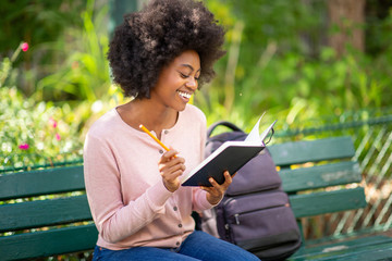 young smiling african american woman sitting outside writing in book