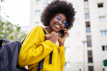 happy young african american woman with glasses and bag walking in city and talking with phone