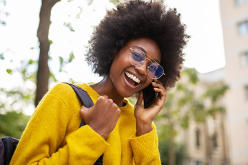 Close up happy young african american woman with glasses and bag walking in city and talking with...