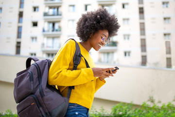 african american woman smiling with glasses and bag walking and talking with cellphone in city