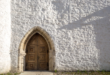 Rough, bumpy and uneven white wall and heavy Gothic wooden door at the entrance to the tower of St. Mary's cathedral (Toomkirik) in Tallinn Estonia old town, on Toompea hill.