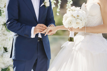 Hands with wedding rings. Modish groom putting a golden ring on the bride's finger during the...