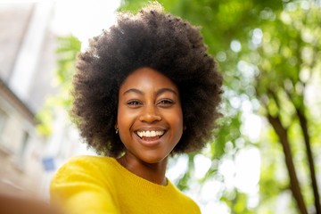 attractive young african american woman with afro taking selfie outside