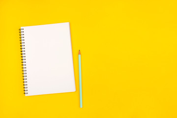 Empty notebook and pencil on yellow background, top view.